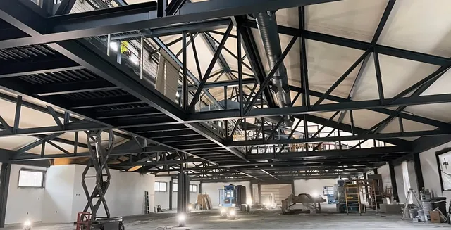 Underside of coated mezzanine framing and roof trusses — lifts and floor protection still in place