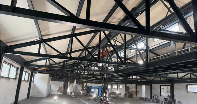 Finished black-coated roof trusses and mezzanine framing in a large interior space