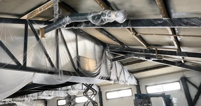 Ductwork, ceiling deck, and mezzanine wrapped in plastic sheeting before blasting and coating the structural steel