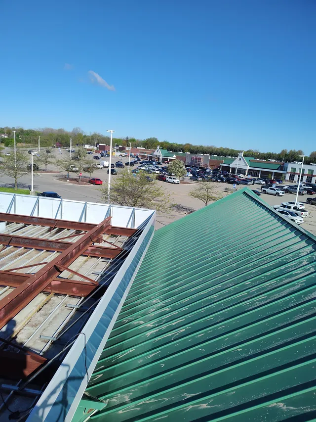 Weathered green standing-seam metal roof on a commercial shopping center before brush blasting